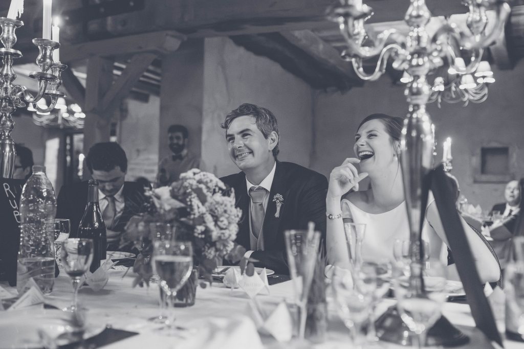 Les mariés riant à la table d'honneur pendant le dîner, chandeliers et bouquet, reportage de mariage en noir et blanc dans la Nièvre