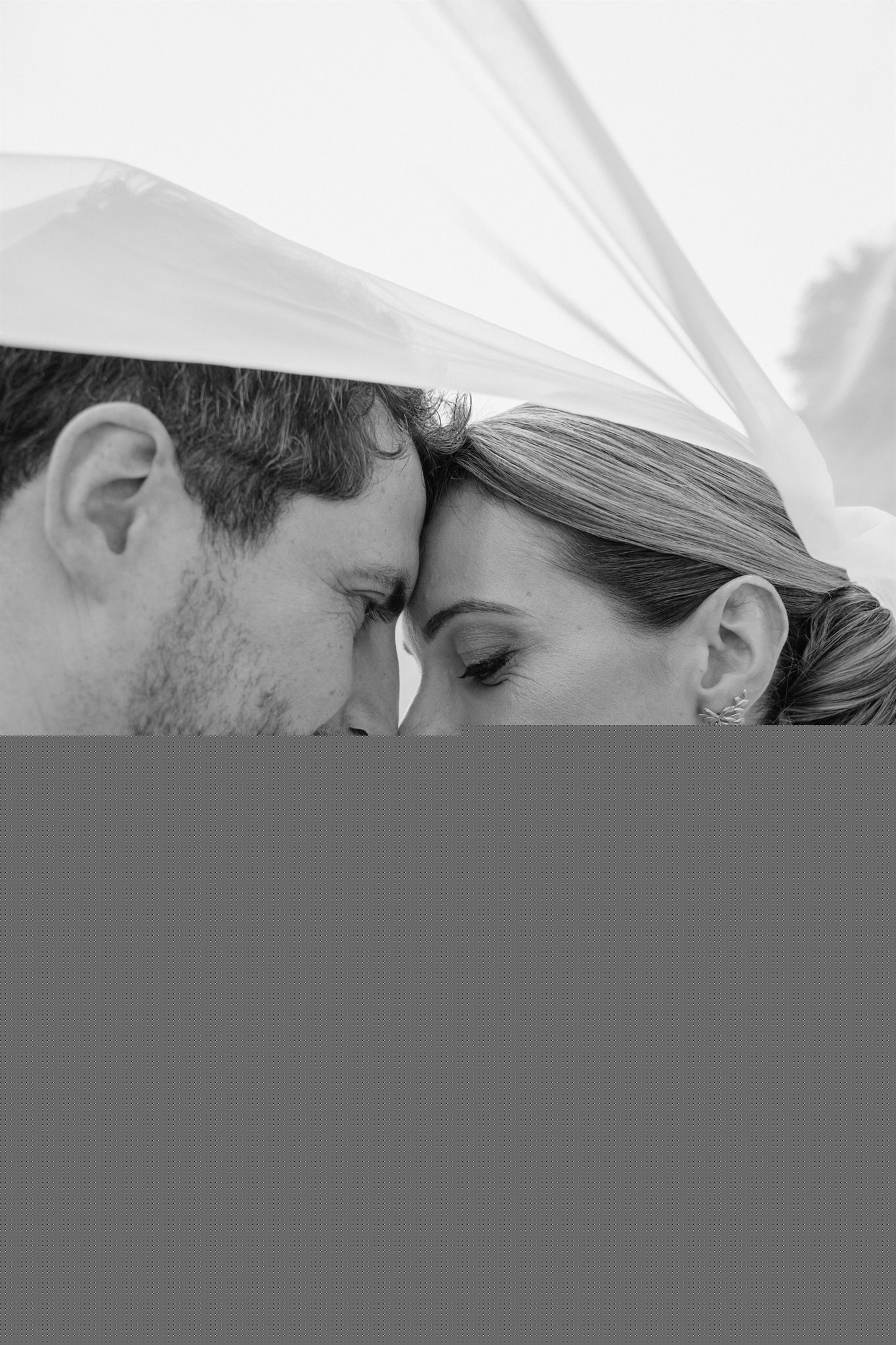 Les mariés front contre front sous le voile, photographie de mariage en noir et blanc