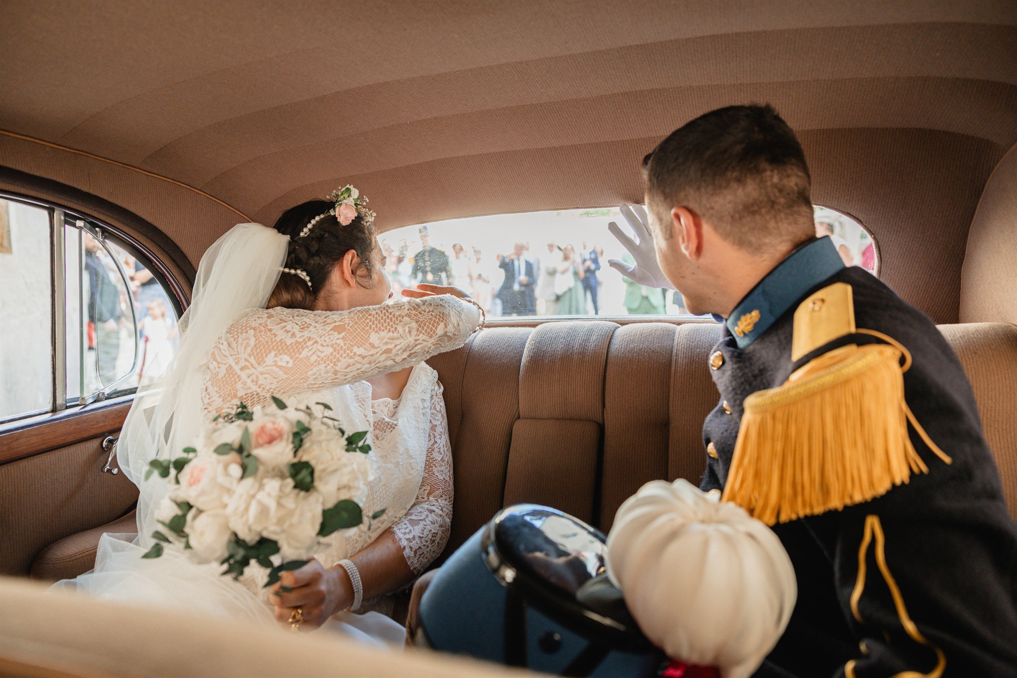 Les mariés saluant leurs invités depuis la banquette d'une voiture ancienne, à la sortie de la cérémonie