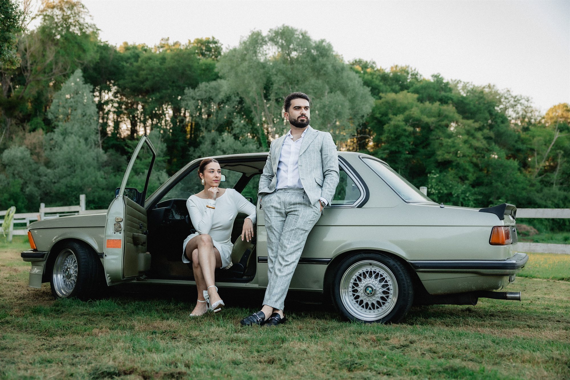 Les mariés devant une BMW ancienne à la lumière du soir