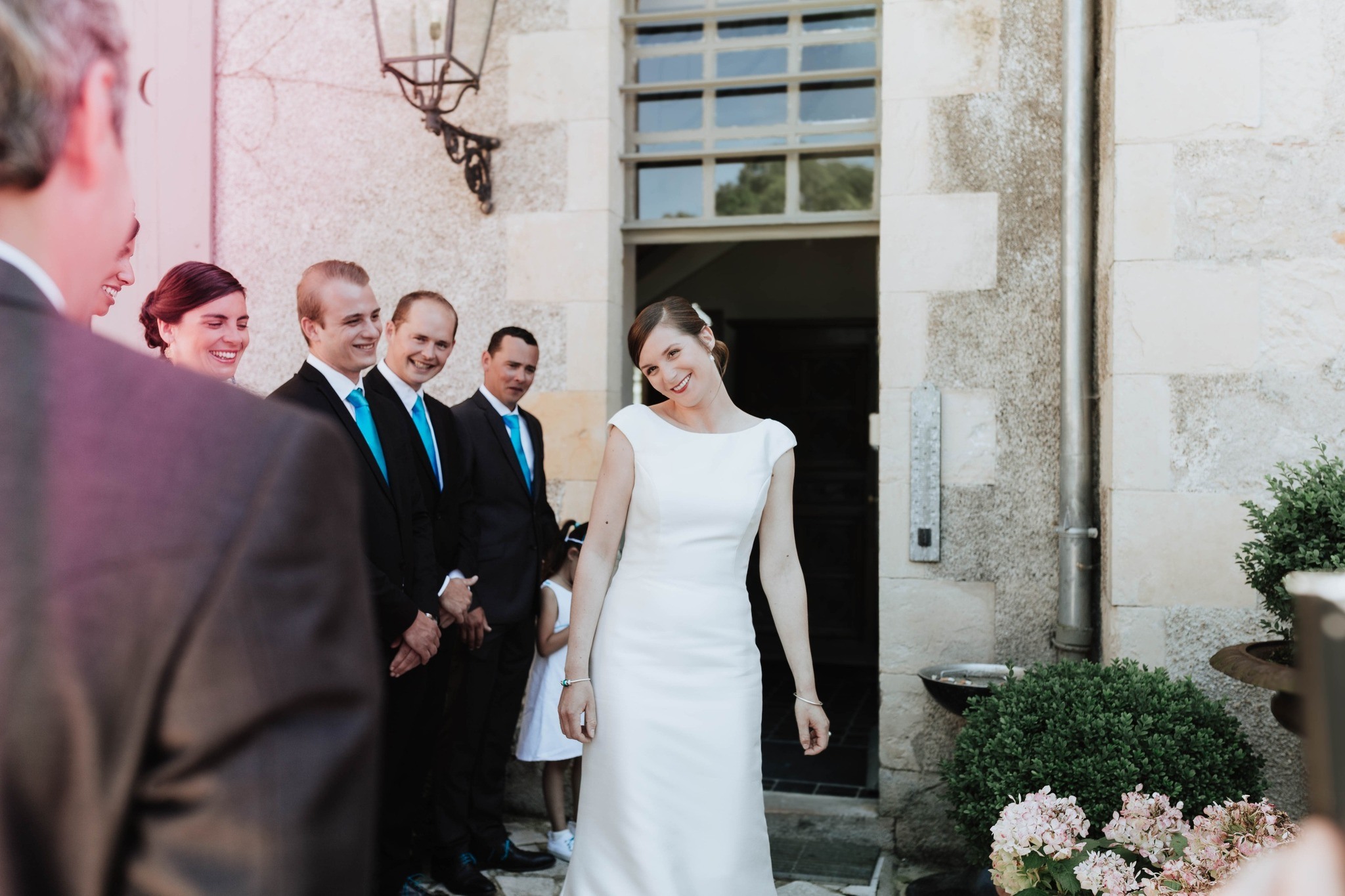 La mariée passant devant ses invités souriants, façade en pierre du Château de Planchevienne