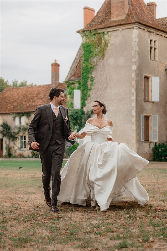 Mariés marchant main dans la main devant un manoir