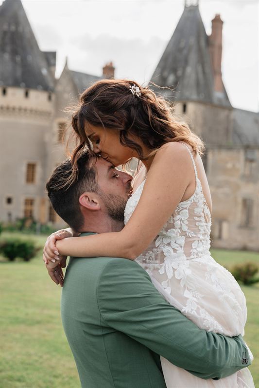 Le marié portant la mariée devant un château